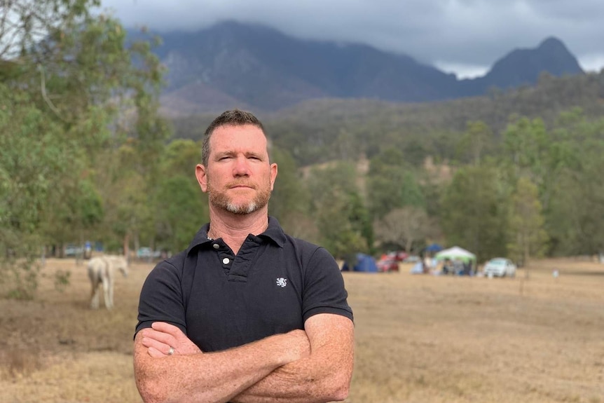 Mr Larkin poses with arms crossed towards camera, in the background is Mount Barney.