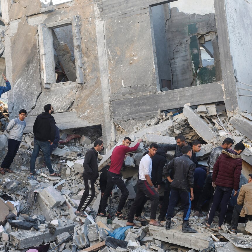 palestinian men and boys stand on a heap of rubble looking for survivors