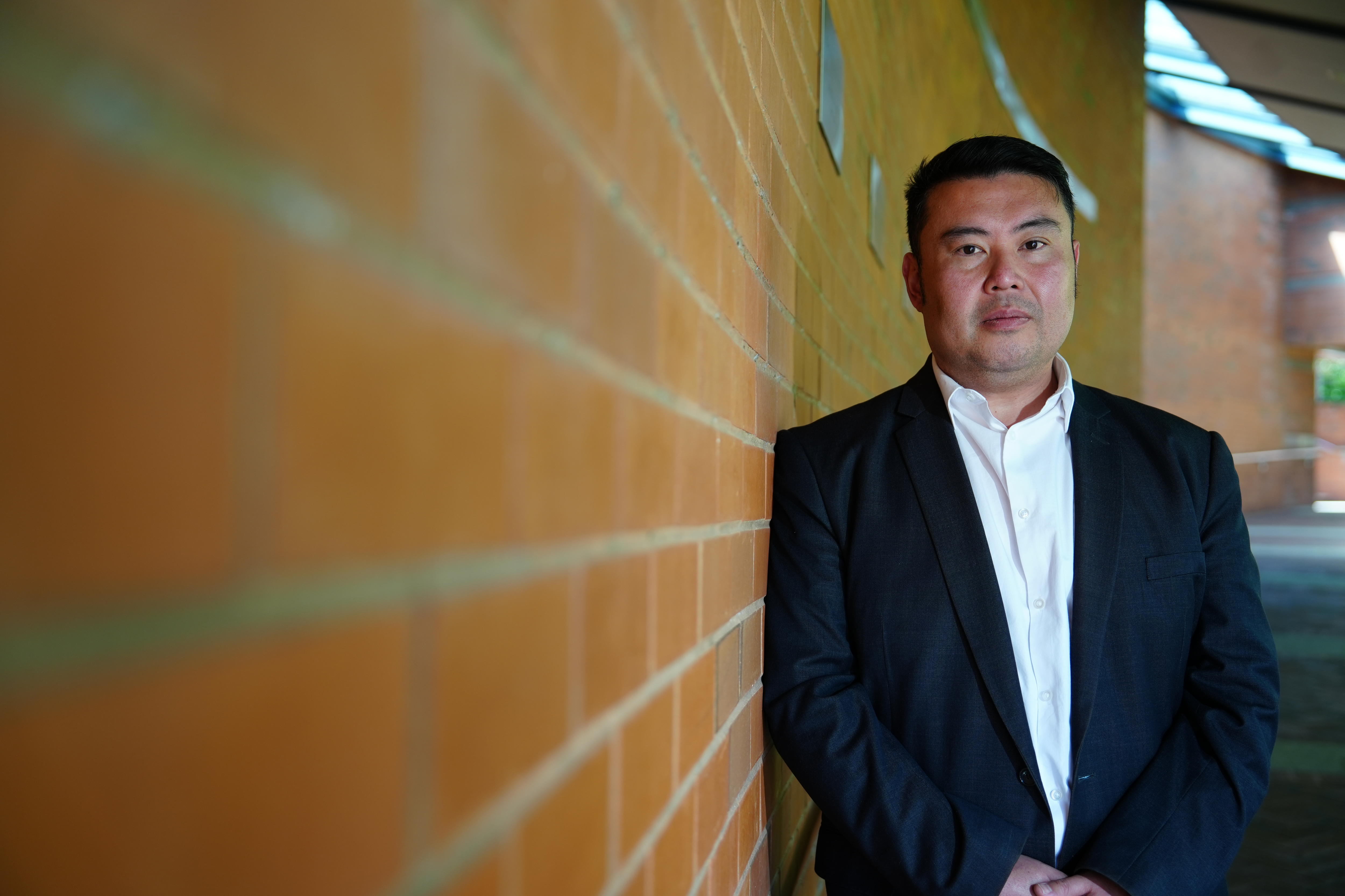 Ian Li stands against a brick wall with a serious expression.