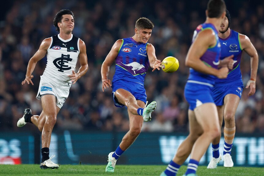 A Kangaroos AFL p[ayer runs and kicks the ball downfield with his right foot.