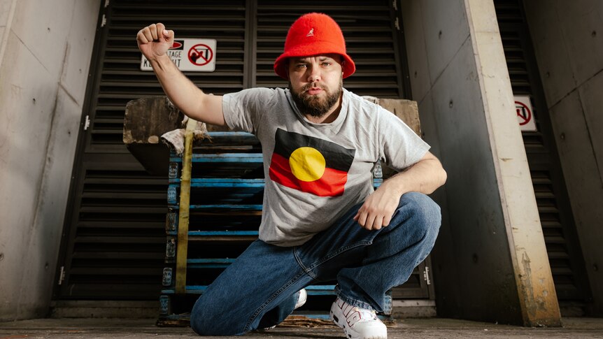 Kai Clancey kneels wearing Aboriginal flag shirt and holding fist in the air