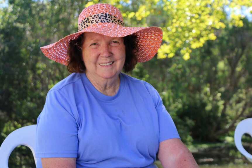 A mid-shot of a woman in a blue shirt and pink hat sitting down.