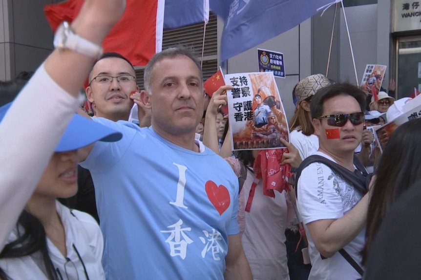 A Caucasian man stands in the middle of a crowd of East Asian people who all don pro-China clothing and face tattoos.