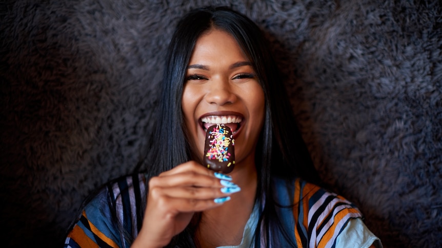 A woman eats a chocolate popsicle covered in sprinkles