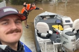 A man in a cap, with a moustache takes a selfie with this boat, while a man bows to it. 