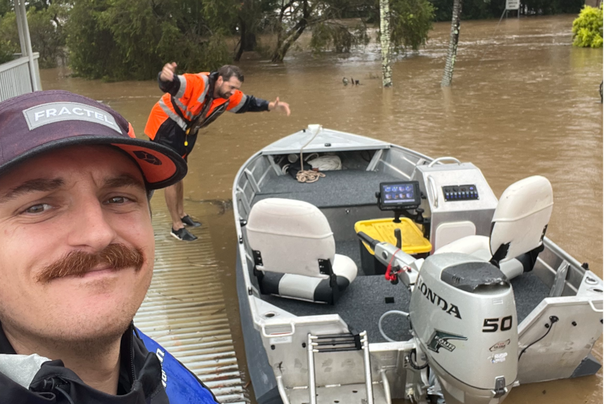 A man in a cap, with a moustache takes a selfie with this boat, while a man bows to it. 