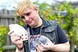 Aaron Ducker smiles while holding a fan of playing cards and a glass ball used for magic tricks. 