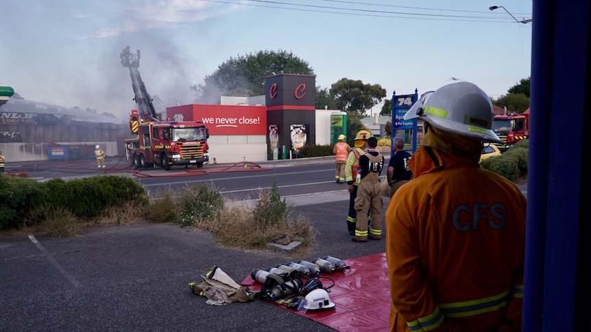 Firemen stand beside firefighting equipment as other crew members fight a blaze at a Mount Barker tyre store across the road.