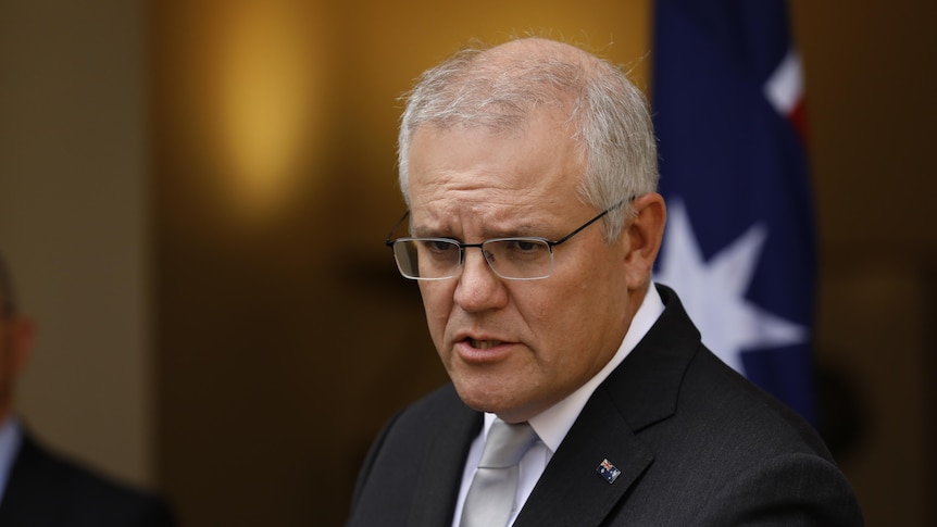 Scott Morrison looks serious while addressing the media in front of an Australian flag