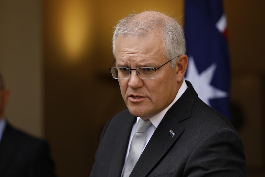 Scott Morrison is serieus als hij met verslaggevers spreekt voor de Australische vlag