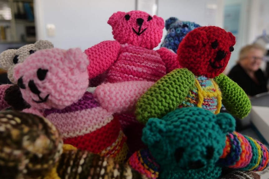 Colourful knitted bears sit in a box on the bench of a medical centre.