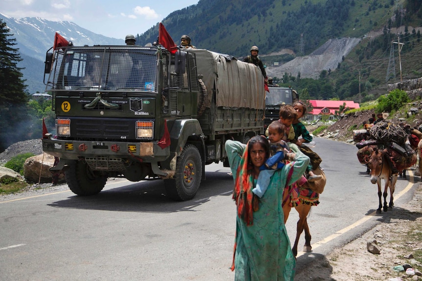 Kashmiri Bakarwal nomads walk with a donkey and children as an Indian army convoy drives past.