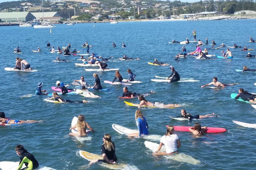 Dozens of people paddling surfboards in a harbour.