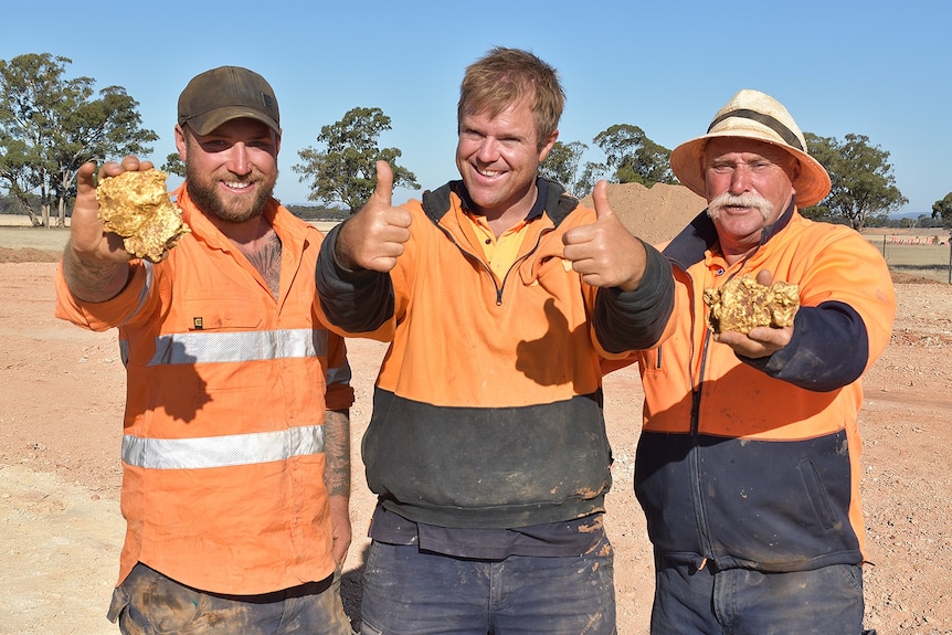 three men in fluorescent clothes hold up gold nuggets