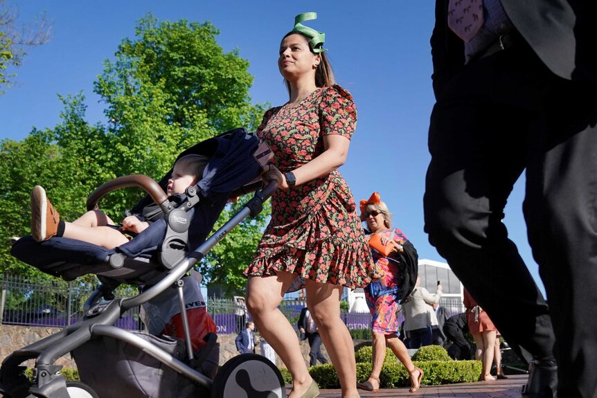 A woman with a child in a pram enter Flemington Racecourse on cup day.