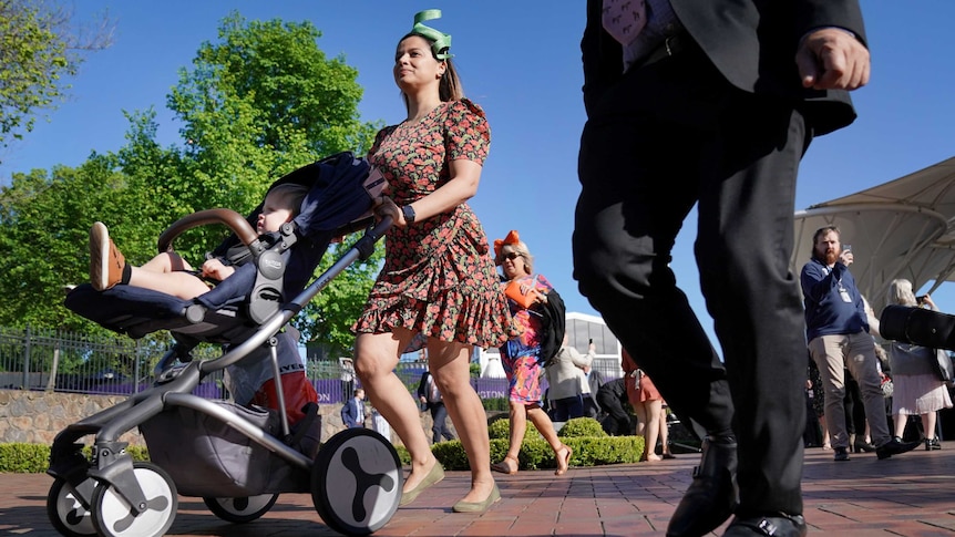 A woman with a child in a pram enter Flemington Racecourse on cup day.