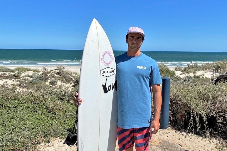man standing at beach holding surfboard