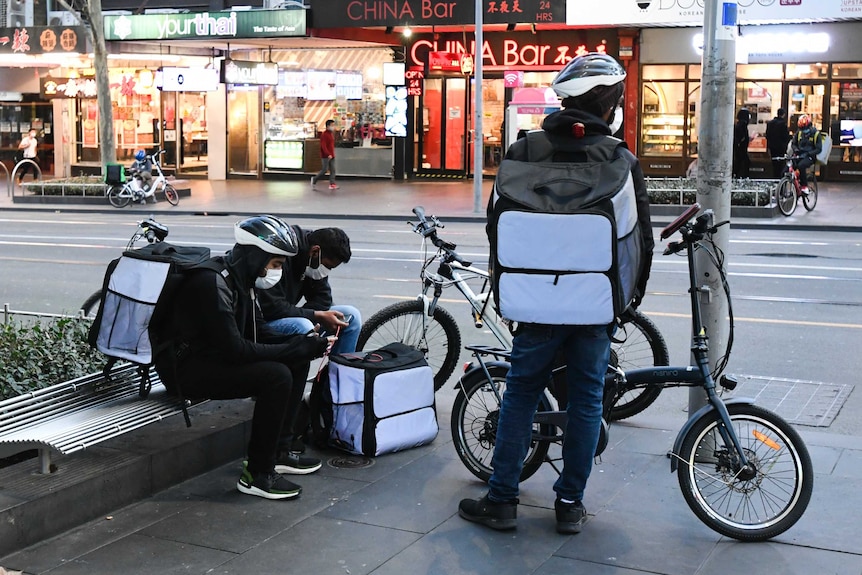 Delivery riders on their bikes in a group on a street sidewalk