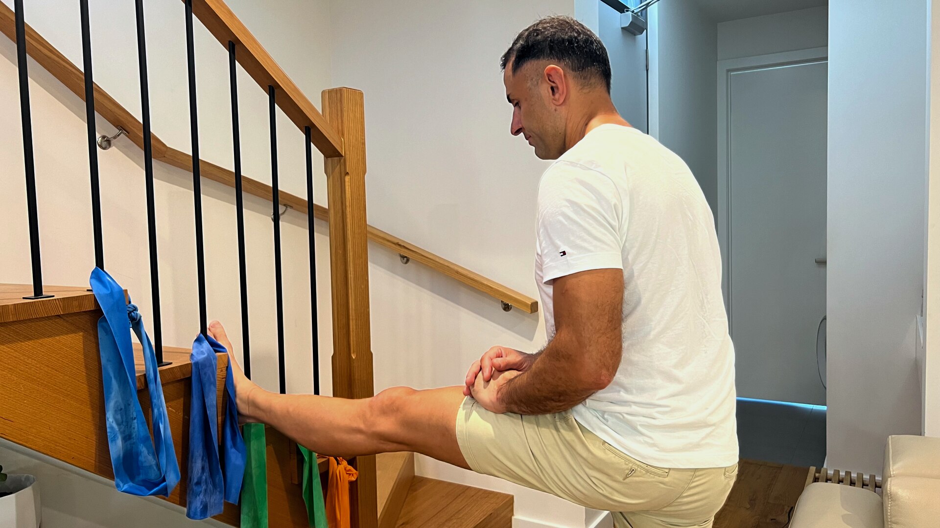 A man stretches his leg on the stairs in a house.