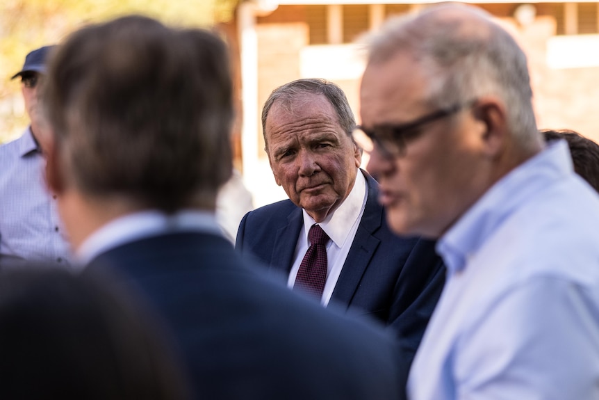 A man wearing a suit listening to the Prime Minister.