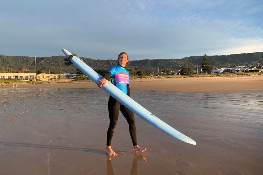 lady holding surfboard on a beach smiling