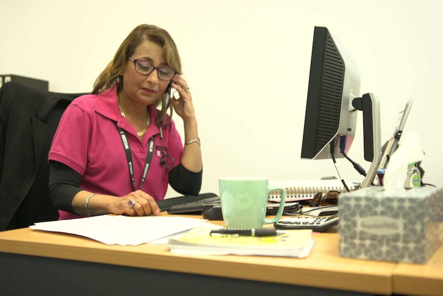 Isis Khalil sits at a computer desk speaking on a phone.