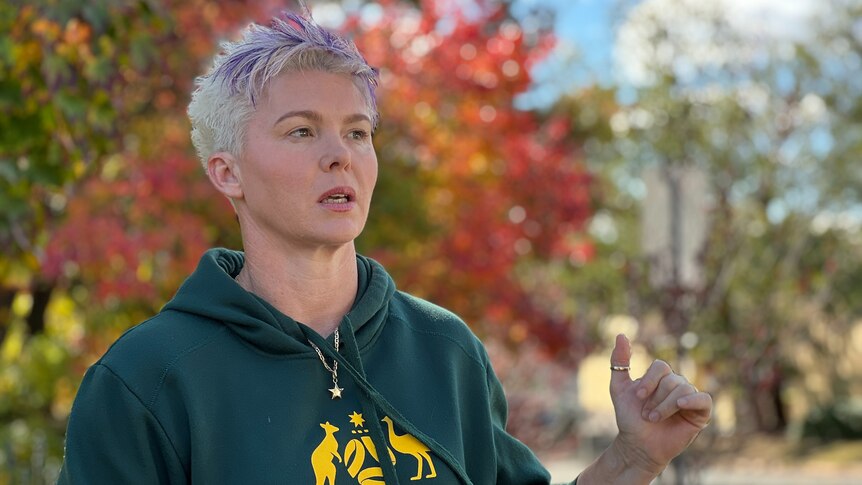 A woman with short hair wearing a Matildas hoodie speaks in front of a microphone