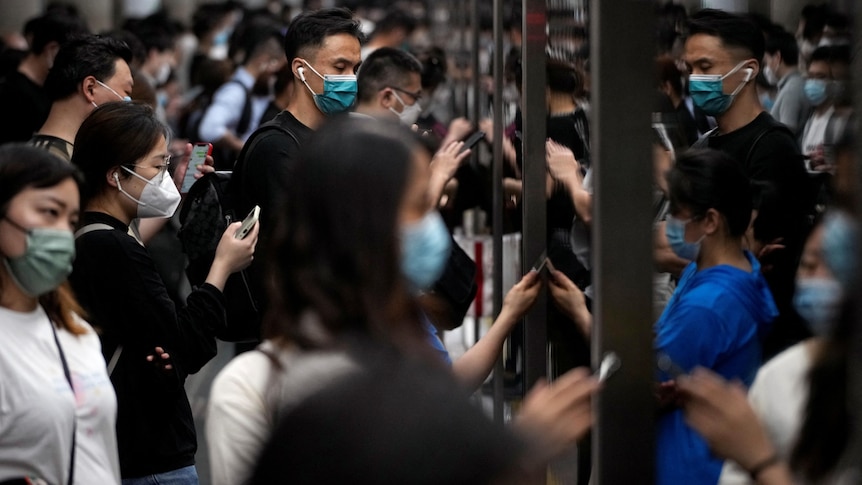 A huge group of masked commuters waiting to enter a train 