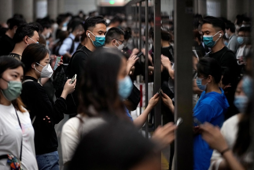 A huge group of masked commuters waiting to enter a train 