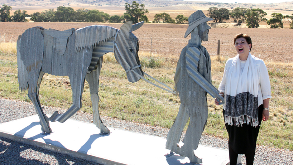 A woman laughing standing next to a corrugated iron statue of a man leading a horse.