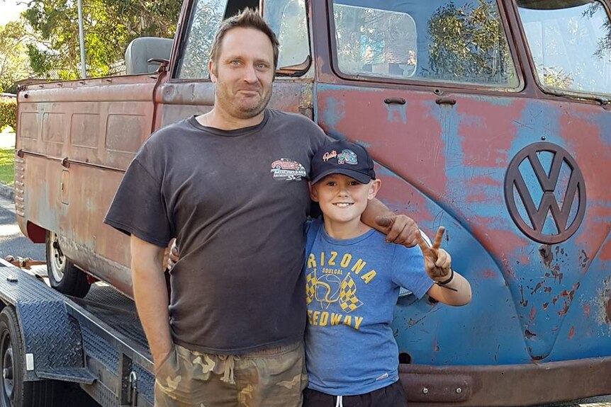 Man and boy stand in front of rusty Kombi