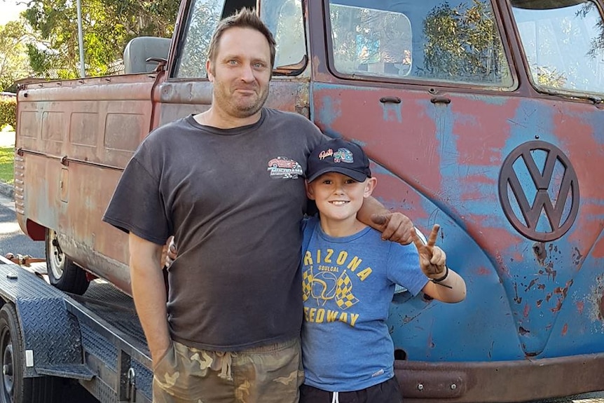 Man and boy stand in front of rusty Kombi