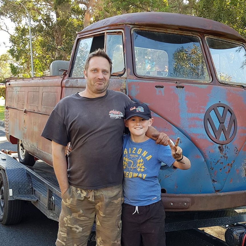 Man and boy stand in front of rusty Kombi