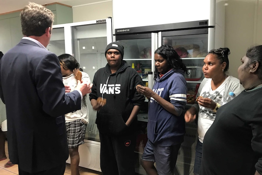 Several women eat cookies with a minister in a kitchen.