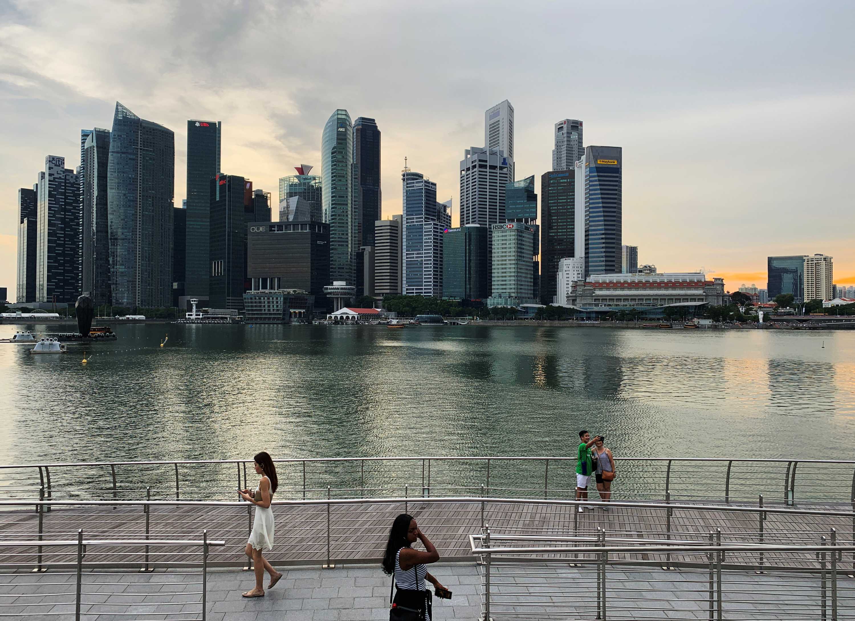 People stand by the harbor in Singapore in front of the city skyline, taking selfies.