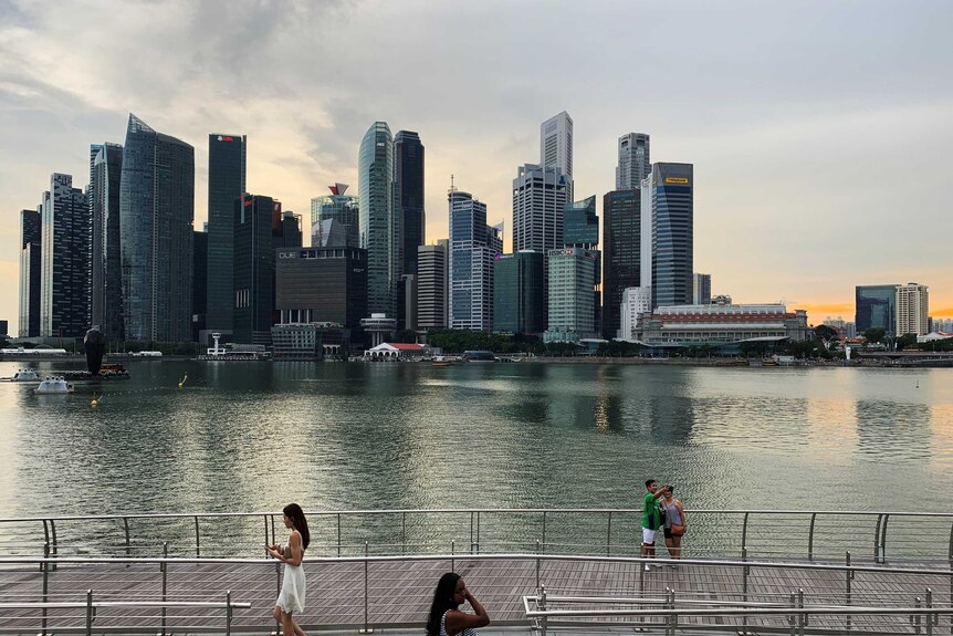 People stand by the foreshore of Singapore harbour in front of the city skyline, taking selfies.