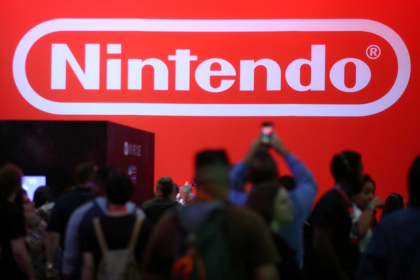 people take photos on their phone as they stand in front of a large red screen with the Nintendo logo on it