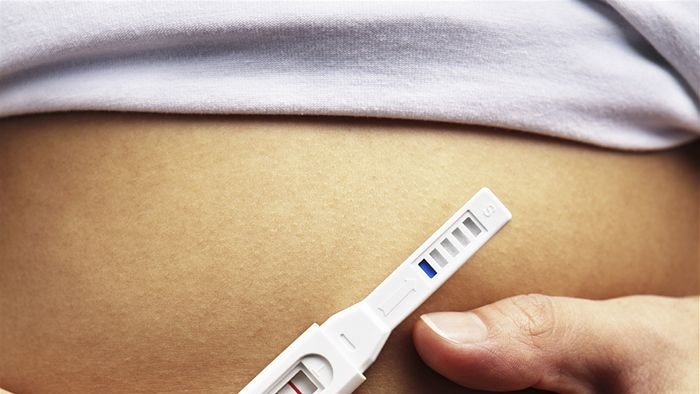 Woman holding a pregnancy test in front of her stomach.