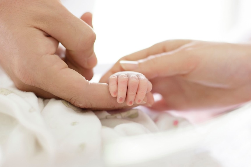 A mother and father hold the hand of their stillborn baby.