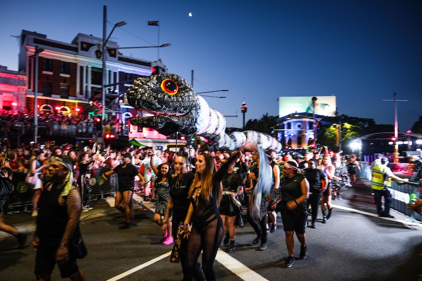 Un grand serpent décoratif est porté dans un défilé le long d'une rue bondée