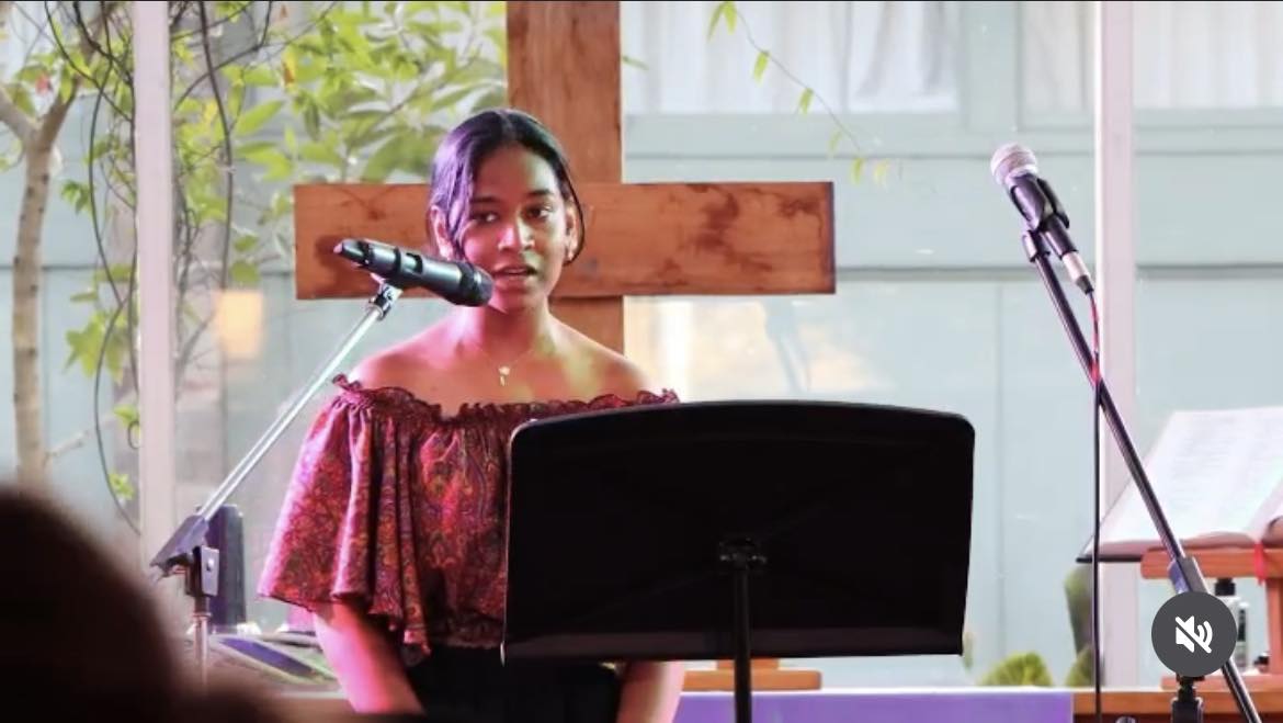 Satara speaking at church, on the stage with a wooden cross behind her.