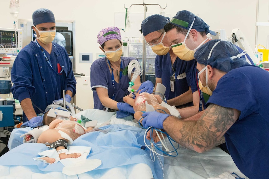 A group of medics with two separate children on an operating table.