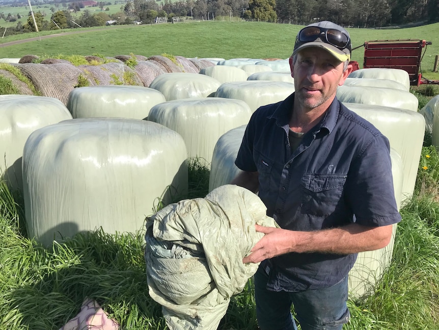 Tasmanian dairy farmer Stuart Burr with plastic wrapped hay bales.