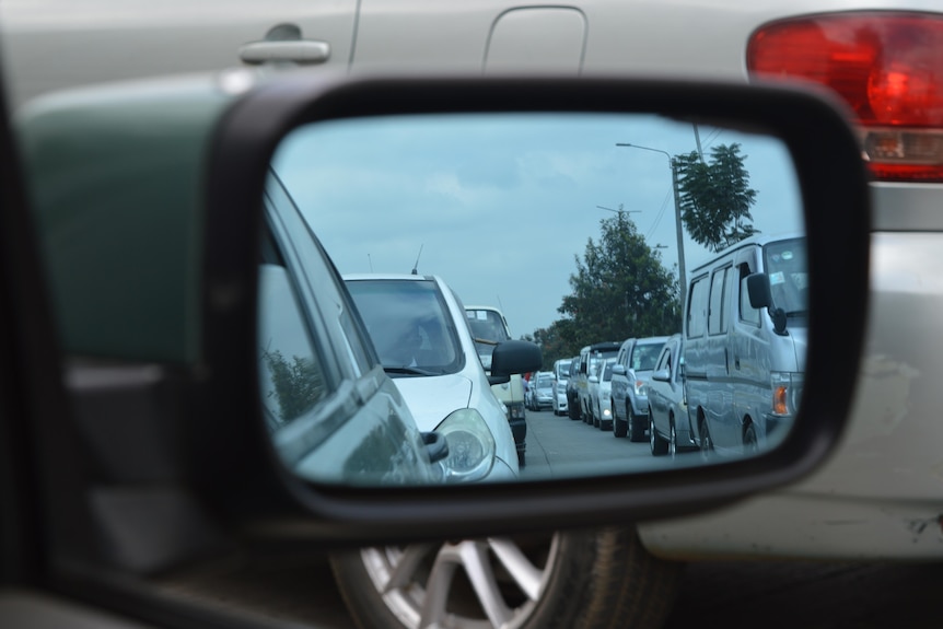A long line of traffic is visible in a cars rear view mirror.