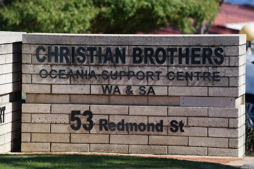 A photo of a low brick wall with black letters and text on it, at the front of a driveway.