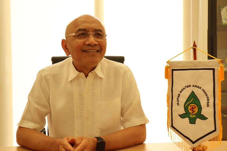 A man wearing glasses sitting with his arms on the table