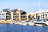 Multi-storey houses line a stretch of water with pleasure boats in the right foreground.