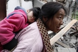 A survivor carries her sleeping daughter as she walks past debris at a village up on the mountainside.