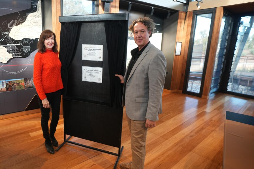 A woman and a man unveil a curtain showing a plaque on a pull-up board