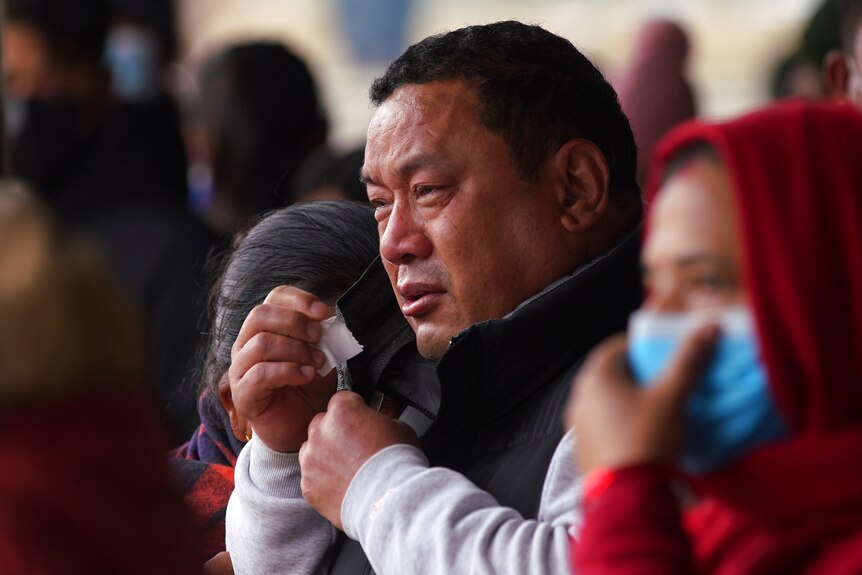 A man looks deeply upset as he cries, holding a tissue in his hand.